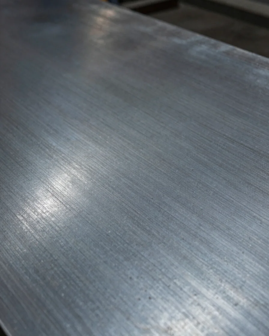 Documentary close-up of a formed steel surface under directional workshop light, visible tooling marks, cool steel tones
